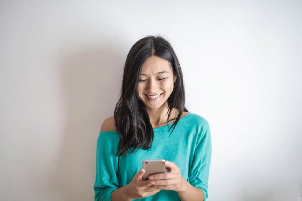 A patient wearing a teal blouse holds a smartphone to illustrate AI text messaging in healthcare.