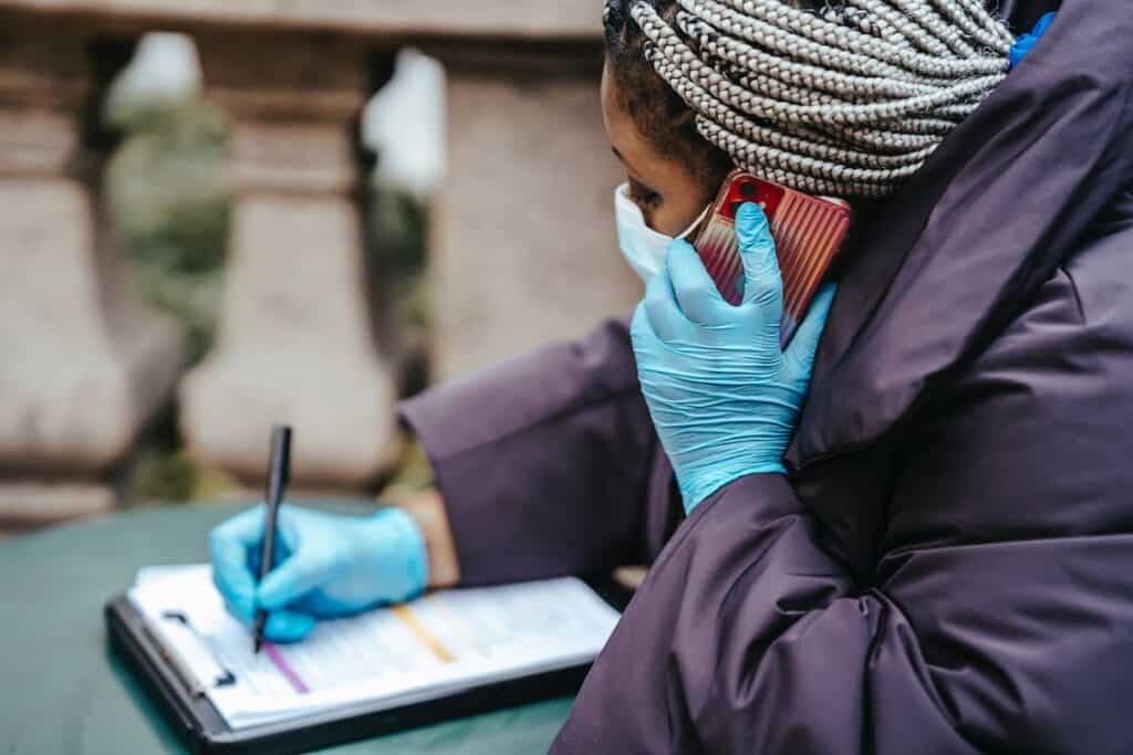A healthcare worker writes on a clipboard and speaks on a smartphone to demonstrate automated communication in healthcare settings.